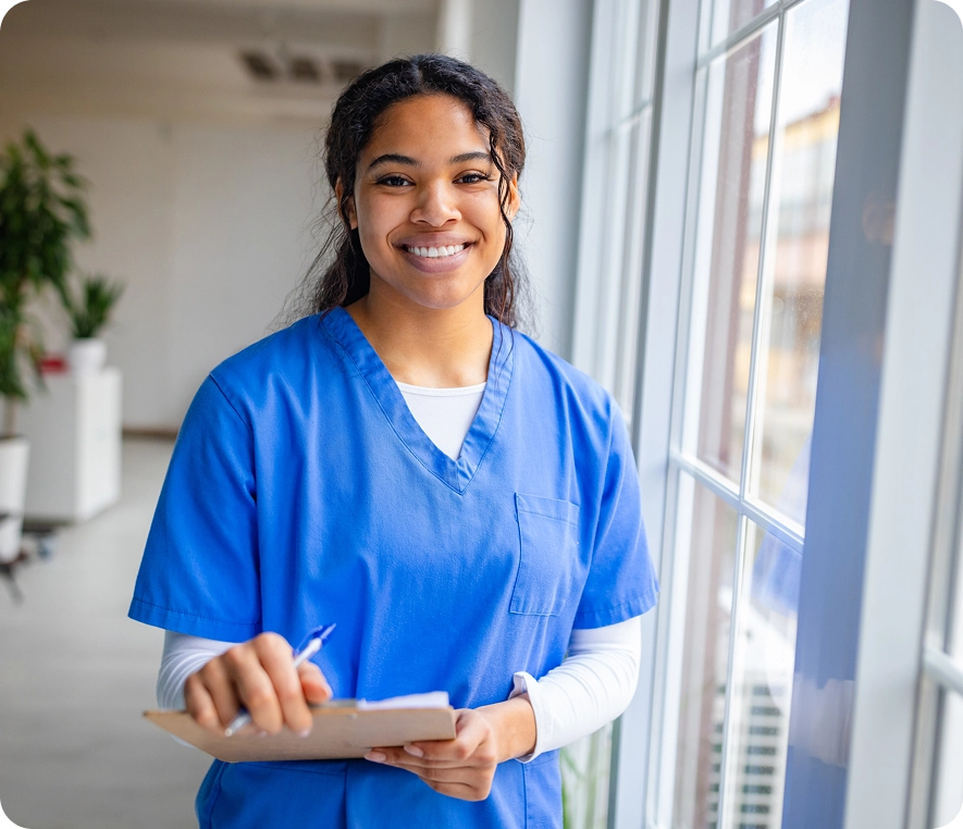 Nurse standing by a window with clipboard.